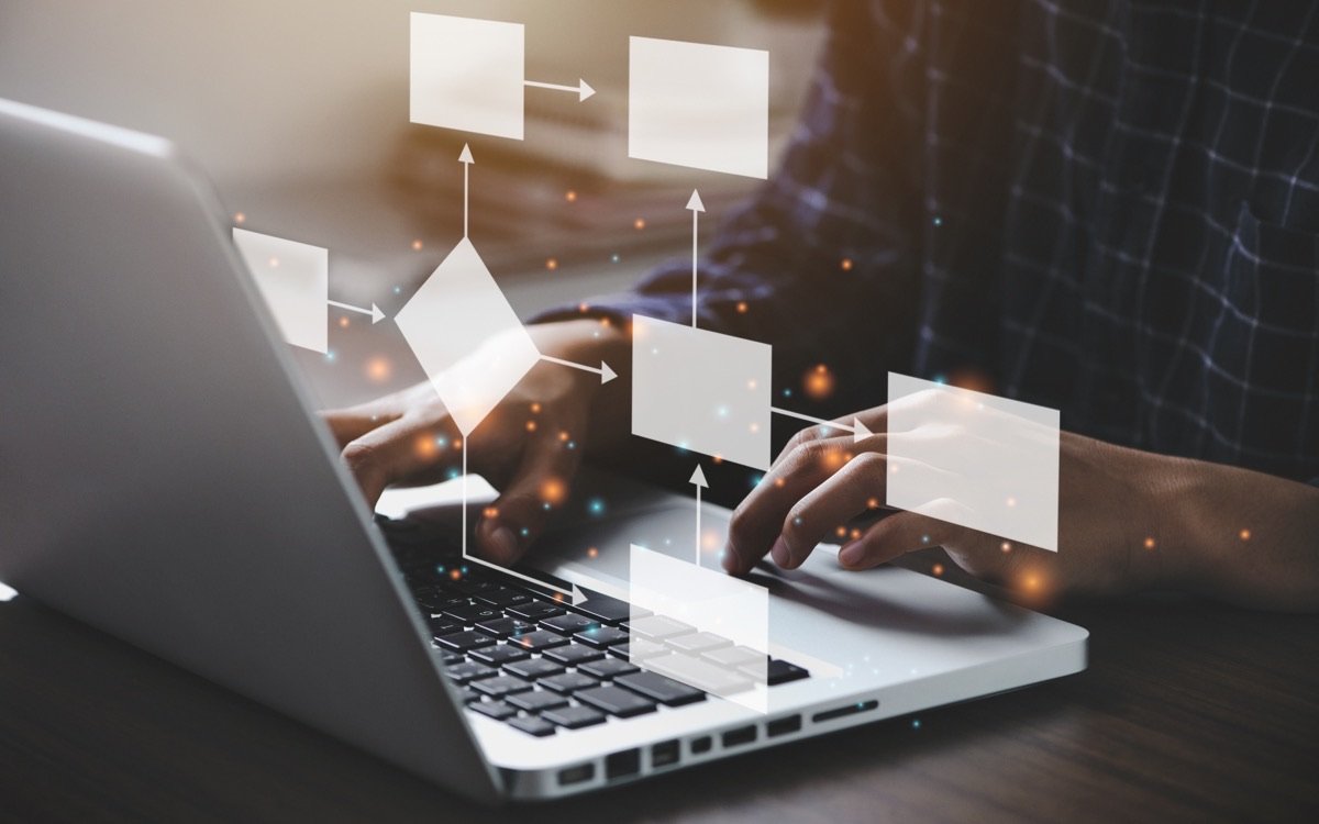 Hands at a laptop with a flow chart of connected process steps above it